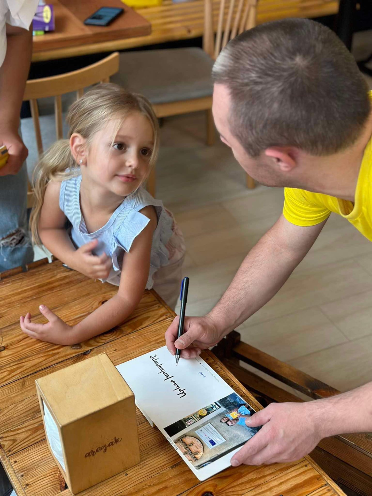 A young girl watching her book get signed at a cafe